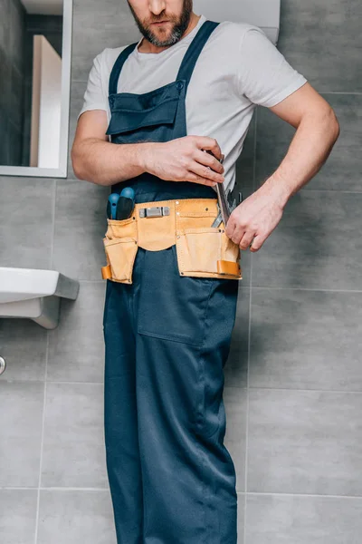 Vue partielle du plombier mâle mettant clé à outils dans la ceinture d'outils dans la salle de bain — Photo de stock