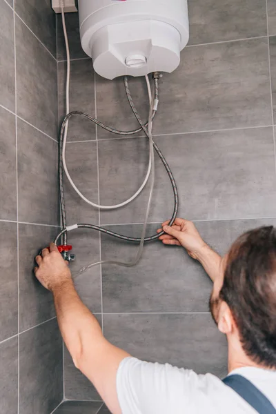 Visão traseira do encanador masculino reparando caldeira elétrica no banheiro — Fotografia de Stock