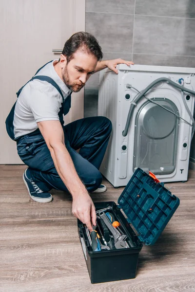 Artesano tomando herramientas de la caja de herramientas durante la reparación de la lavadora en el baño - foto de stock