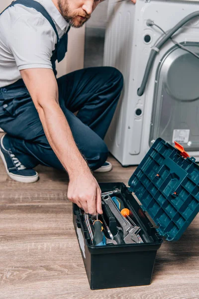 Recortado tiro de artesano tomando herramientas de la caja de herramientas durante la reparación de la lavadora en el baño - foto de stock