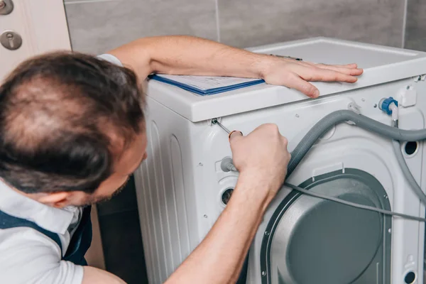 Messa a fuoco selettiva del tuttofare maschio che ripara la lavatrice in bagno — Foto stock