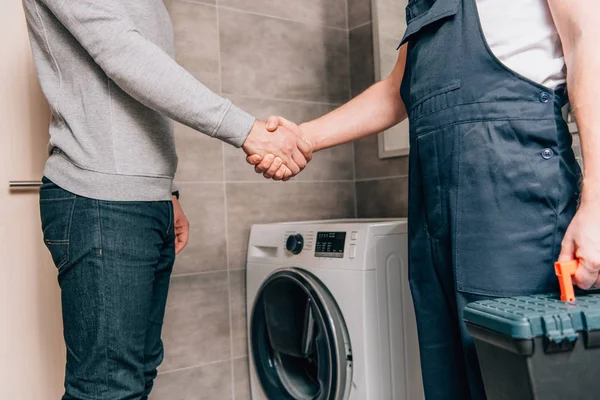 Cropped image of male handyman with toolbox shaking hands with owner in bathroom — Stock Photo