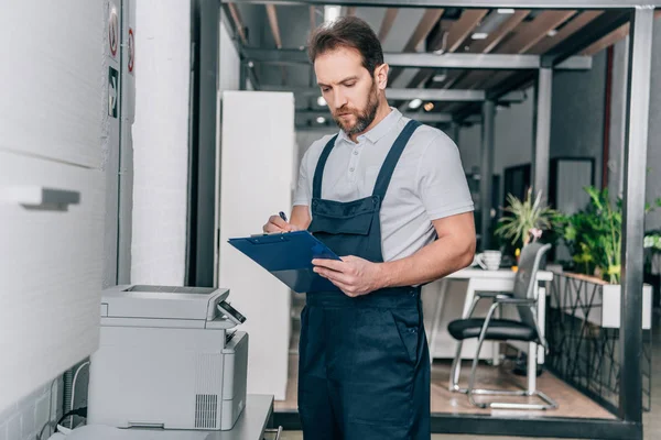 Handwerker checkt Kopiergerät und schreibt in Klemmbrett in modernem Büro — Stockfoto