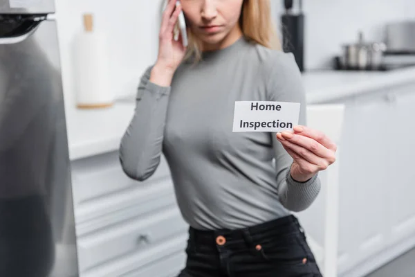 Teilbild einer jungen Frau, die eine Karte mit Schriftzug nach Hause hält und in der Küche mit dem Smartphone spricht — Stockfoto