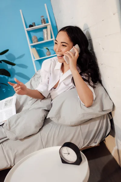 Attraktive asiatische Frau spricht per Smartphone und lacht im Schlafzimmer — Stockfoto