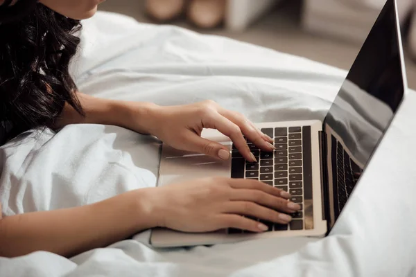 Recortado disparo de mujer joven utilizando el ordenador portátil con pantalla en blanco en la cama - foto de stock