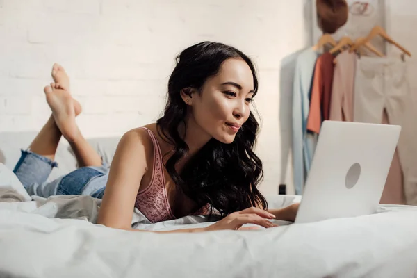 Atractiva mujer asiática acostada en la cama y el uso de ordenador portátil - foto de stock