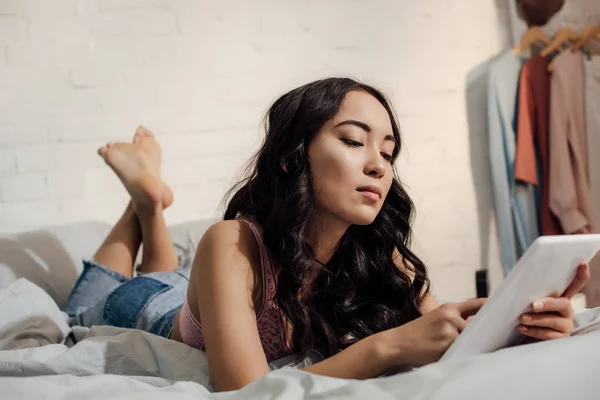 Красивая молодая женщина, лежащая на кровати и использующая планшетный компьютер — стоковое фото