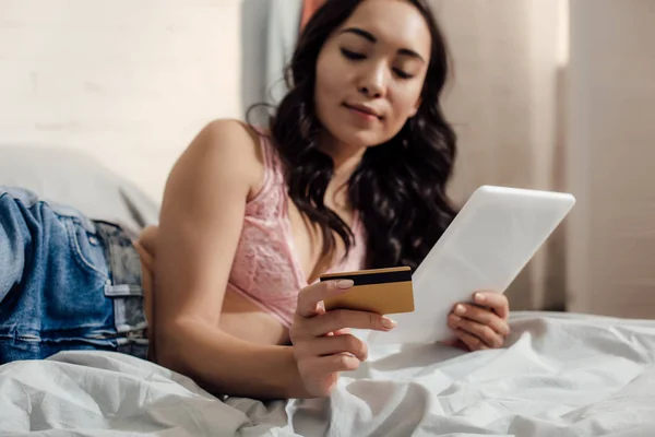 Hermosa joven asiática mujer de compras en línea con digital tablet y tarjeta de crédito en el dormitorio - foto de stock