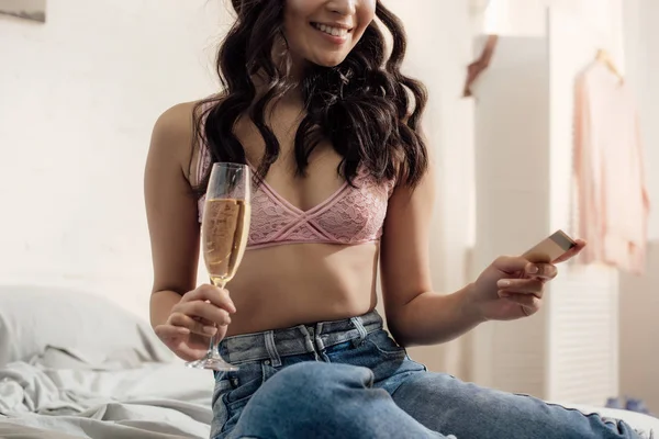 Обрізаний знімок усміхненої молодої жінки, що тримає келих вина та кредитної картки в спальні — стокове фото