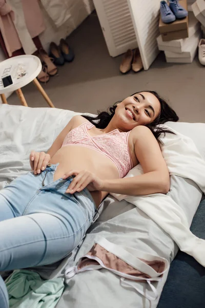 Bela sorrindo asiático menina deitado no cama e colocando no jeans — Fotografia de Stock