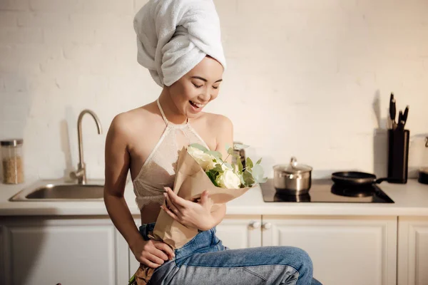 Surpris heureux asiatique fille avec serviette sur la tête tenant bouquet de fleurs blanches roses à la maison — Photo de stock