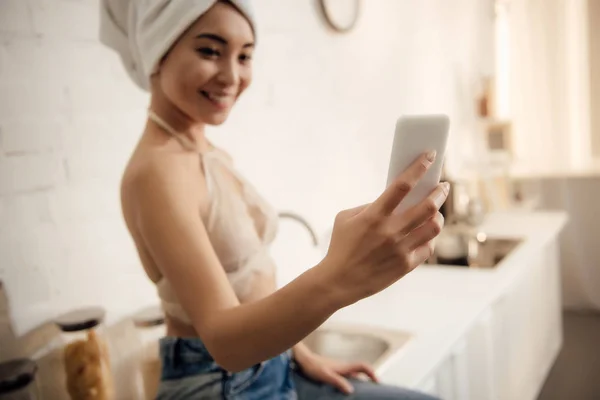 Bela feliz asiático menina com toalha na cabeça tomando selfie com smartphone na cozinha — Fotografia de Stock