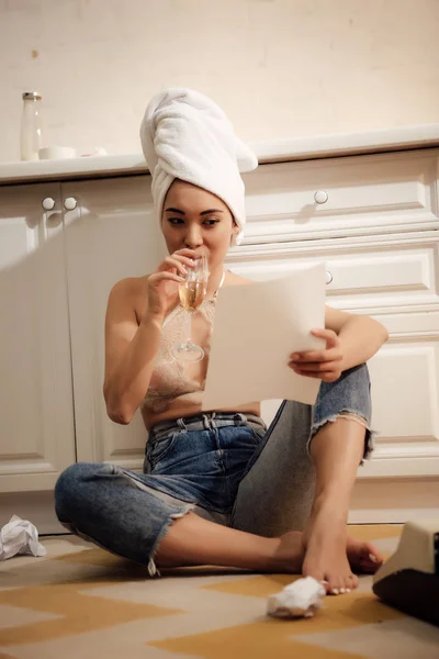 Bella giovane donna con asciugamano sulla testa bere vino e leggere dalla carta a casa — Foto stock