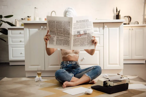 Junge Autorin sitzt auf dem Boden und versteckt Gesicht hinter Wirtschaftszeitung — Stockfoto