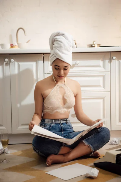 Menina atraente com toalha na cabeça sentado no chão e ler jornal — Fotografia de Stock