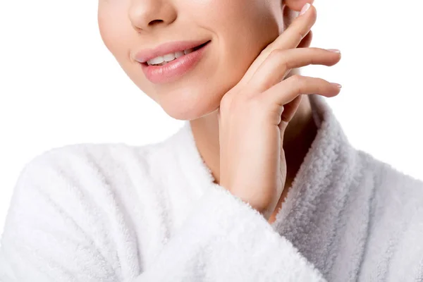 Visão parcial da mulher sorridente em roupão de banho tocando rosto isolado no branco — Fotografia de Stock