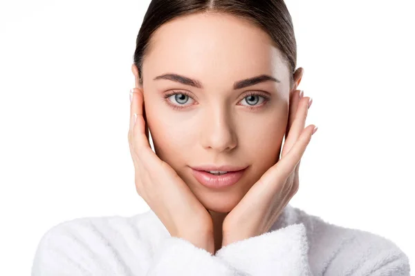 Beautiful woman in bathrobe touching face and looking at camera isolated on white — Stock Photo