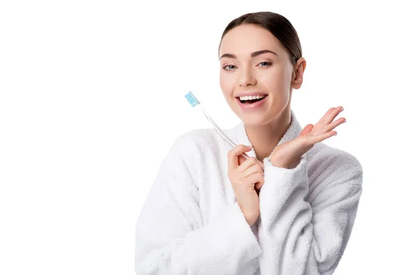 Mujer alegre en albornoz blanco sosteniendo el cepillo de dientes y mirando a la cámara aislada en blanco - foto de stock