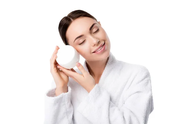 Woman in bathrobe with eyes closed holding face cream isolated on white — Stock Photo