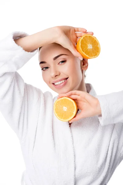 Hermosa mujer sonriente en albornoz blanco sosteniendo naranjas aisladas en blanco - foto de stock