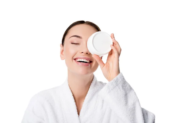 Mujer alegre en albornoz celebración crema hidratante en frente de la cara aislada en blanco - foto de stock