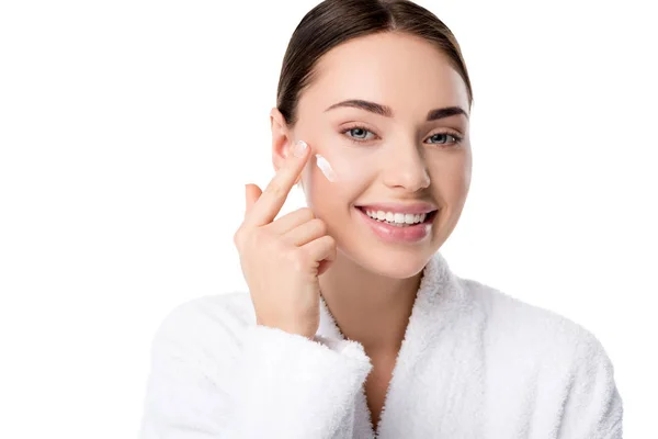 Beautiful woman applying moisturizing face cream and looking at camera isolated on white — Stock Photo