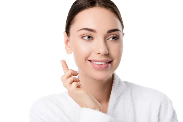 Hermosa mujer sonriente en albornoz con crema facial en la mano aislado en blanco - foto de stock