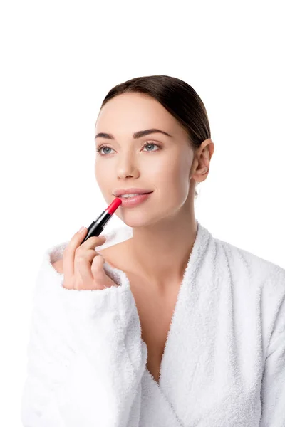 Schöne Frau im Bademantel, die roten Lippenstift isoliert auf weiß aufträgt — Stockfoto