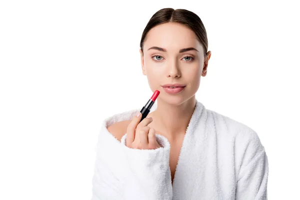 Beautiful woman in bathrobe holding red lipstick and looking at camera isolated on white — Stock Photo