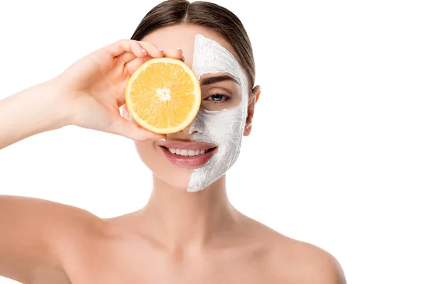 Jolie femme souriante avec masque de soins de la peau du visage tenant orange devant le visage isolé sur blanc — Photo de stock