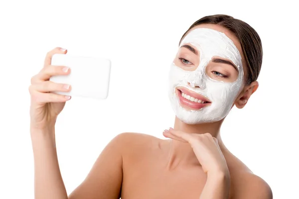 Mujer con mascarilla facial para el cuidado de la piel tomando selfie en smartphone aislado en blanco - foto de stock