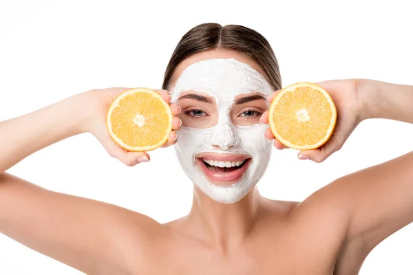 Красивая улыбающаяся женщина с маской ухода за кожей лица, держащая апельсины и глядя на камеру, изолированную на белом — стоковое фото