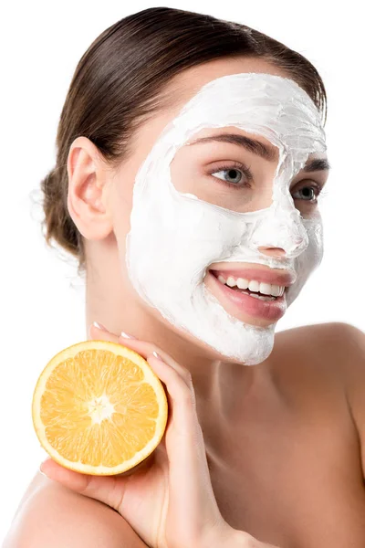 Hermosa mujer sonriente con máscara facial cuidado de la piel sosteniendo naranja aislado en blanco - foto de stock