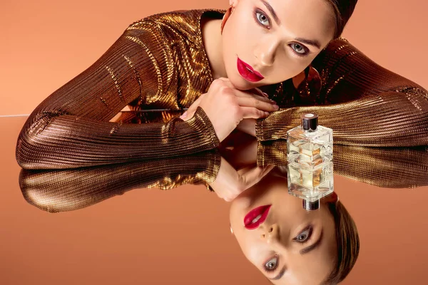Beautiful woman with glamorous makeup, perfume bottle and mirror reflection posing isolated on orange — Stock Photo