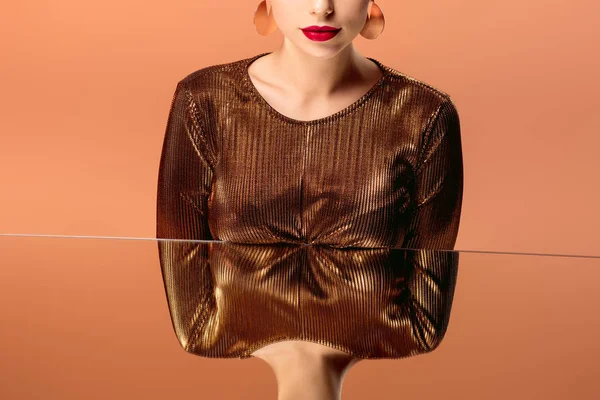 Abgeschnittene Ansicht einer Frau in goldener Kleidung mit roten Lippen und Spiegelreflexion isoliert auf orange — Stockfoto