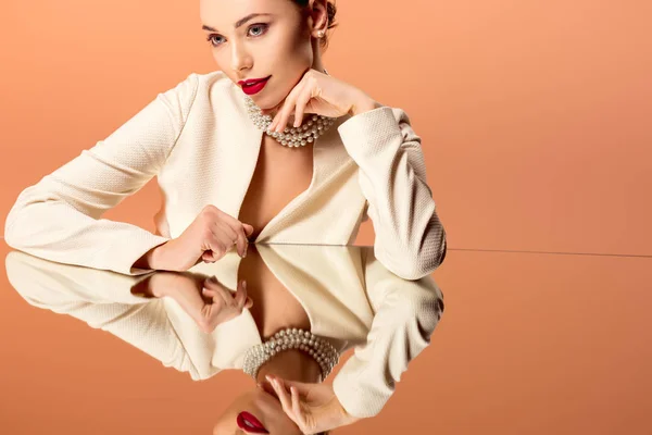 Hermosa mujer en collar de perlas con espejo reflexión posando aislado en naranja — Stock Photo