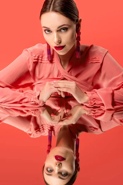 Hermosa mujer en blusa con reflejo de espejo mirando a la cámara aislada en coral vivo - foto de stock