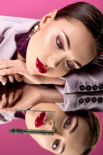 Hermosa mujer glamorosa en ropa formal con labios rojos que reflejan en espejos aislados en rosa - foto de stock
