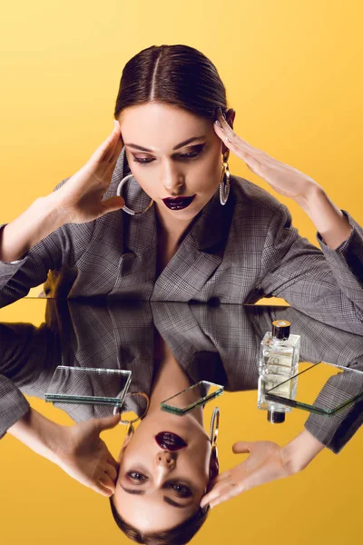 Hermosa mujer glamorosa en desgaste formal con reflejo de espejo y frasco de perfume posando aislado en amarillo - foto de stock