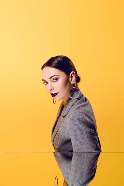 Glamouröse Frau in formeller Kleidung mit Spiegelreflexion, die auf gelb isoliert in die Kamera blickt — Stockfoto
