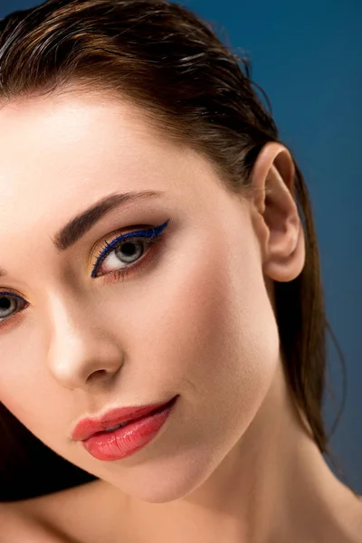 Retrato de mujer atractiva con maquillaje glamoroso mirando a la cámara aislada en azul - foto de stock