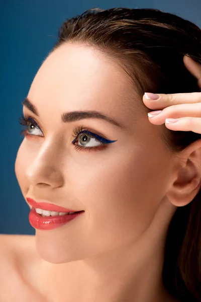 Retrato de bela mulher sorridente com maquiagem glamourosa tocando rosto isolado no azul — Fotografia de Stock
