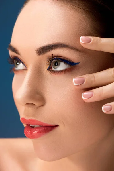 Retrato de mujer hermosa con glamoroso maquillaje tocando la cara aislado en azul - foto de stock