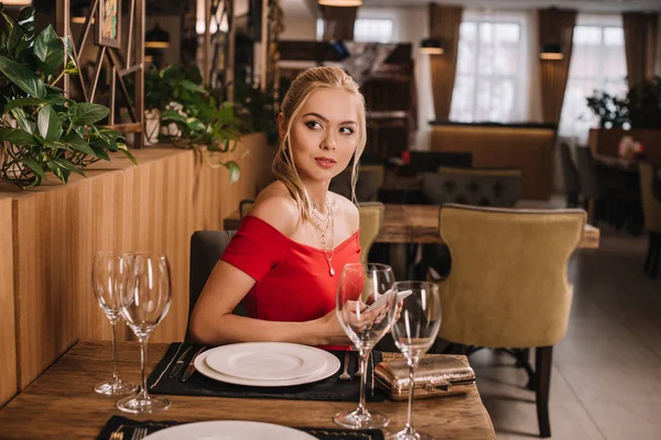 Atractiva mujer en vestido rojo sentado en el restaurante - foto de stock