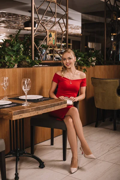 Mulher atraente em vestido vermelho sentado no restaurante e olhando para a câmera — Fotografia de Stock