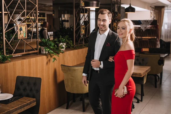 Couple of handsome boyfriend and attractive girlfriend in red dress smiling and walking in restaurant — Stock Photo