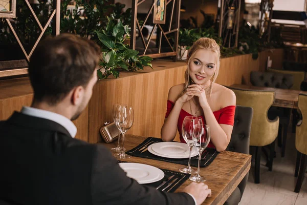 Namorada atraente em vestido vermelho olhando para o namorado no restaurante — Fotografia de Stock