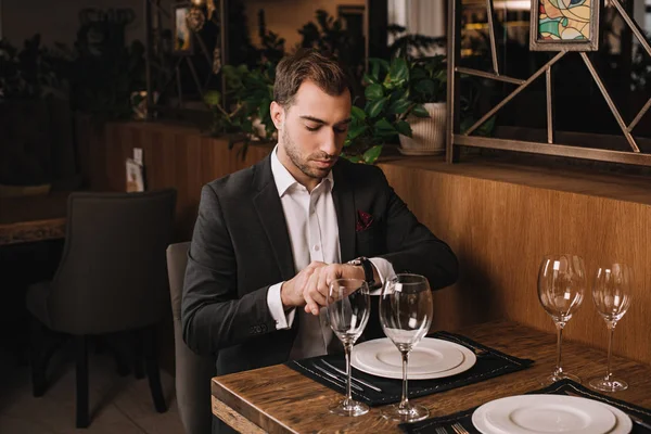 Handsome man in suit waiting for girlfriend in restaurant and looking at watch — Stock Photo