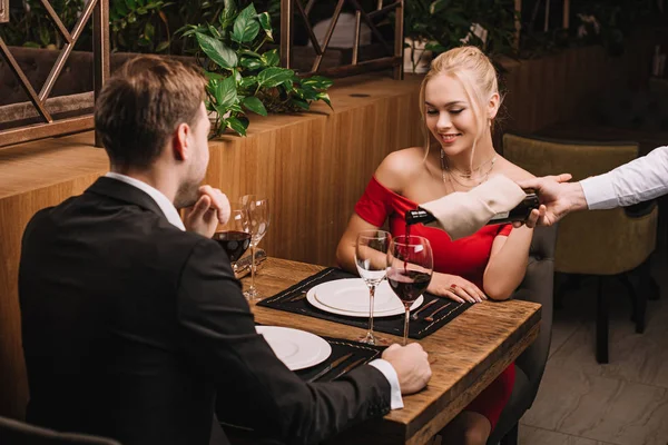 Hombre de traje y chica atractiva en vestido rojo sonriendo y mirando platos - foto de stock